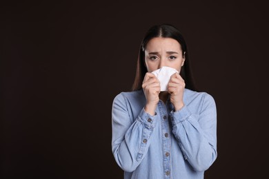 Photo of Young woman blowing nose in tissue on dark background, space for text. Cold symptoms