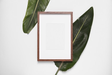 Photo of Empty photo frame and green leaves on white background, top view. Space for design