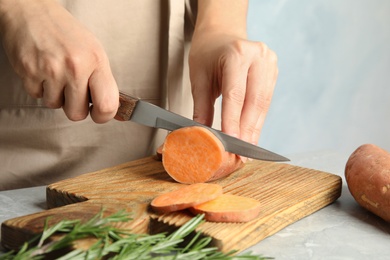 Photo of Woman cutting sweet potato on wooden board, closeup