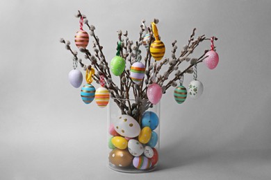 Photo of Vase with beautiful willow branches and painted Easter eggs on light grey background