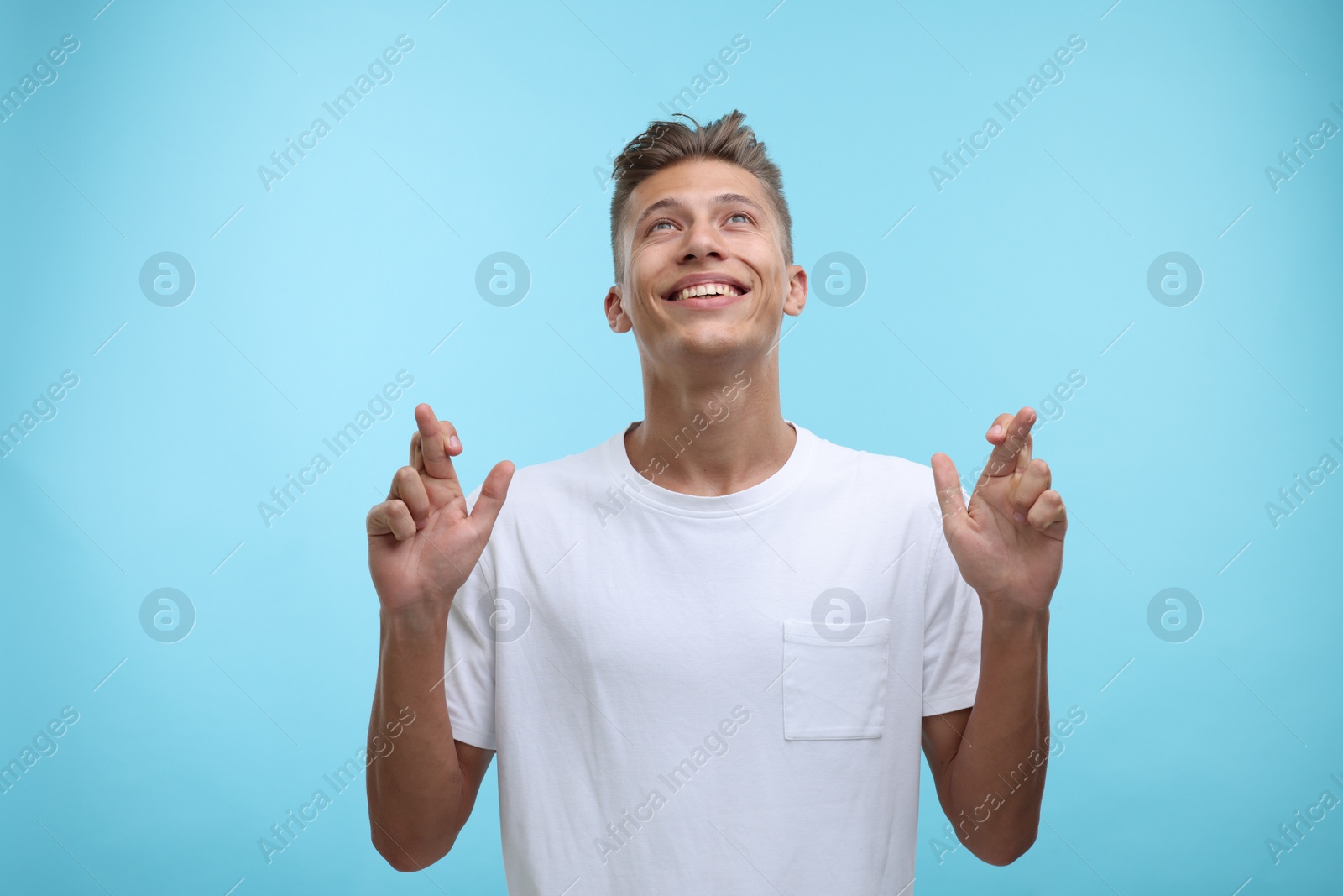 Photo of Emotional young man crossing his fingers on light blue background