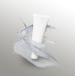 Splashes of cosmetic product and tube with space for design on grey gradient background