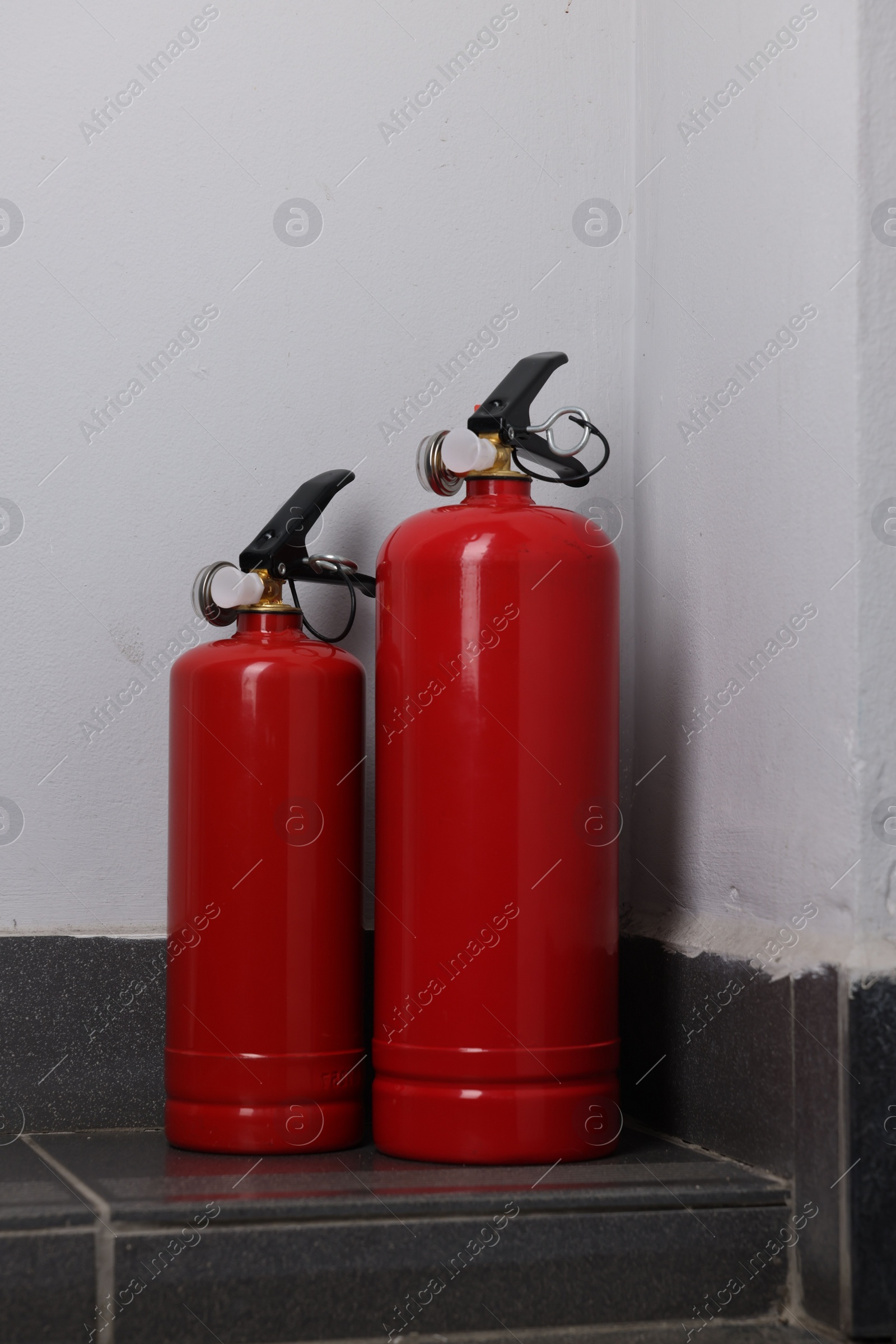 Photo of Two fire extinguishers on floor near white wall