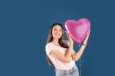 Portrait of young woman with heart shaped balloon on color background. Space for text