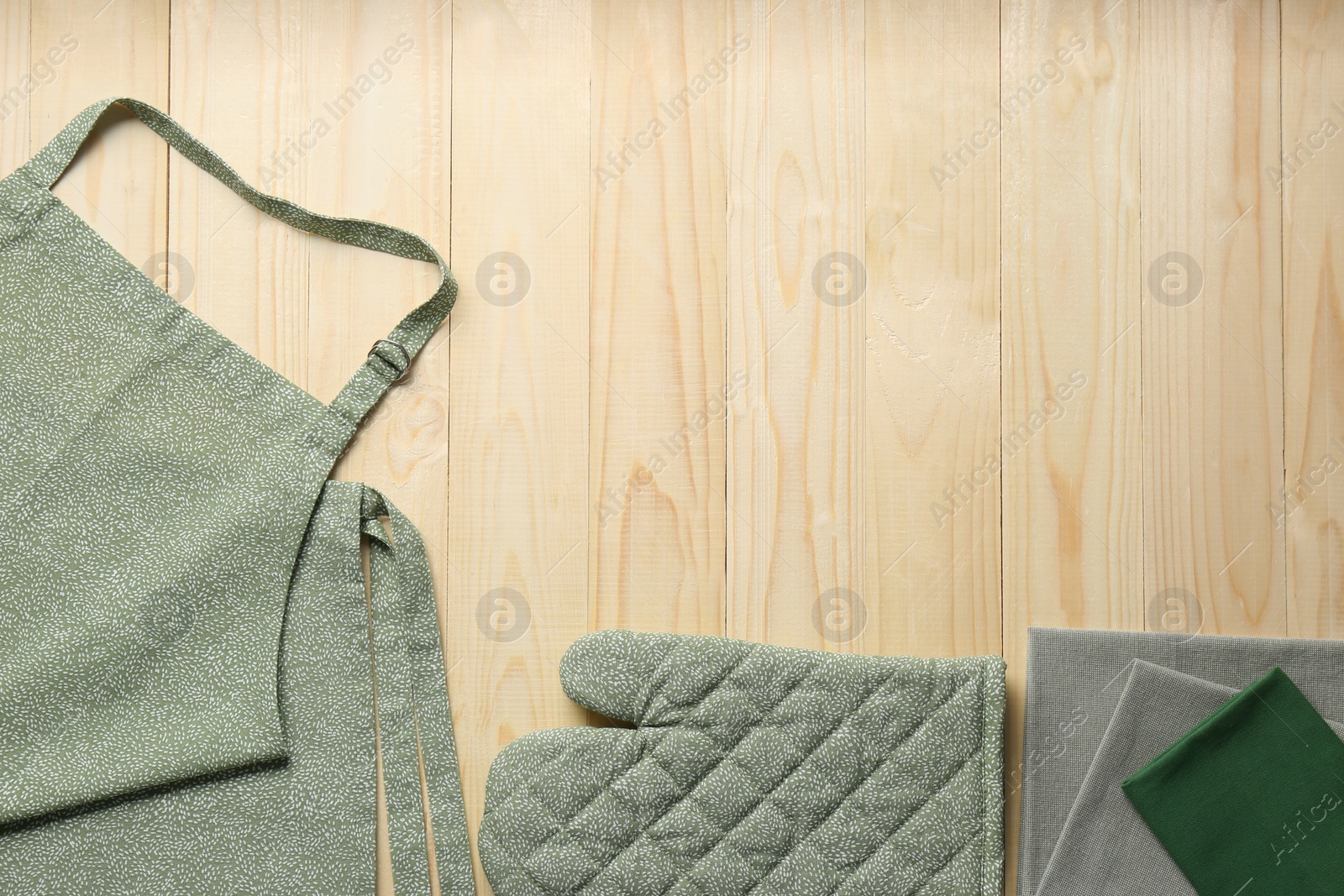 Photo of Kitchen napkins, apron and glove on wooden table, flat lay. Space for text