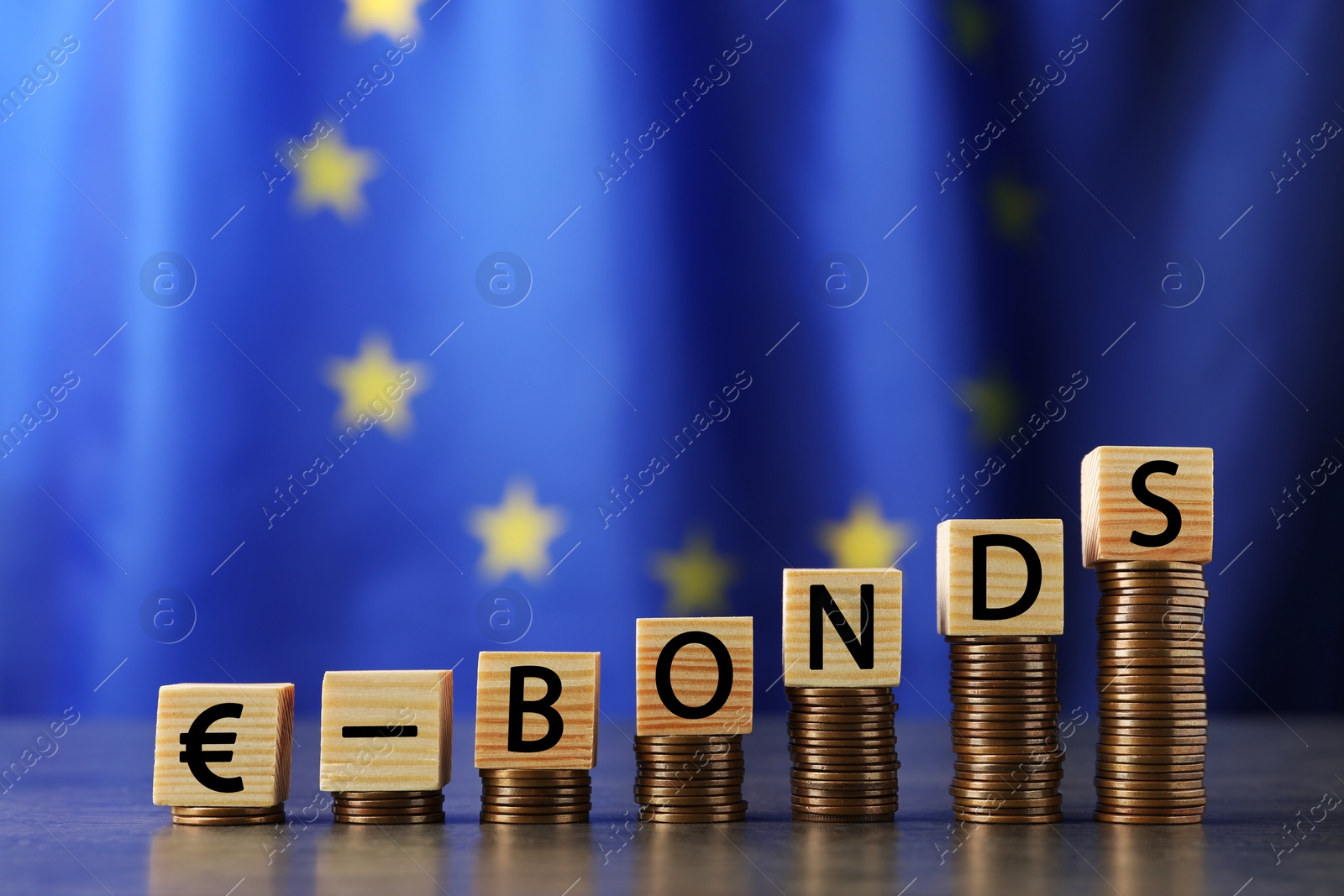 Photo of Stacked coins and word Eurobonds made of wooden cubes with letters on grey table against European union flag