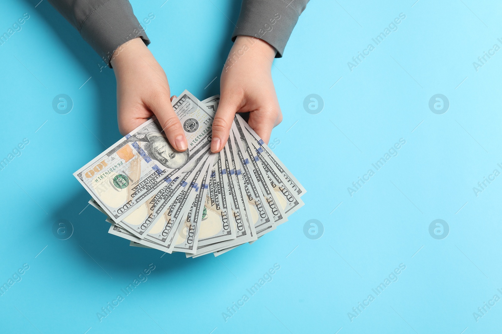 Photo of Money exchange. Woman holding dollar banknotes on light blue background, top view. Space for text