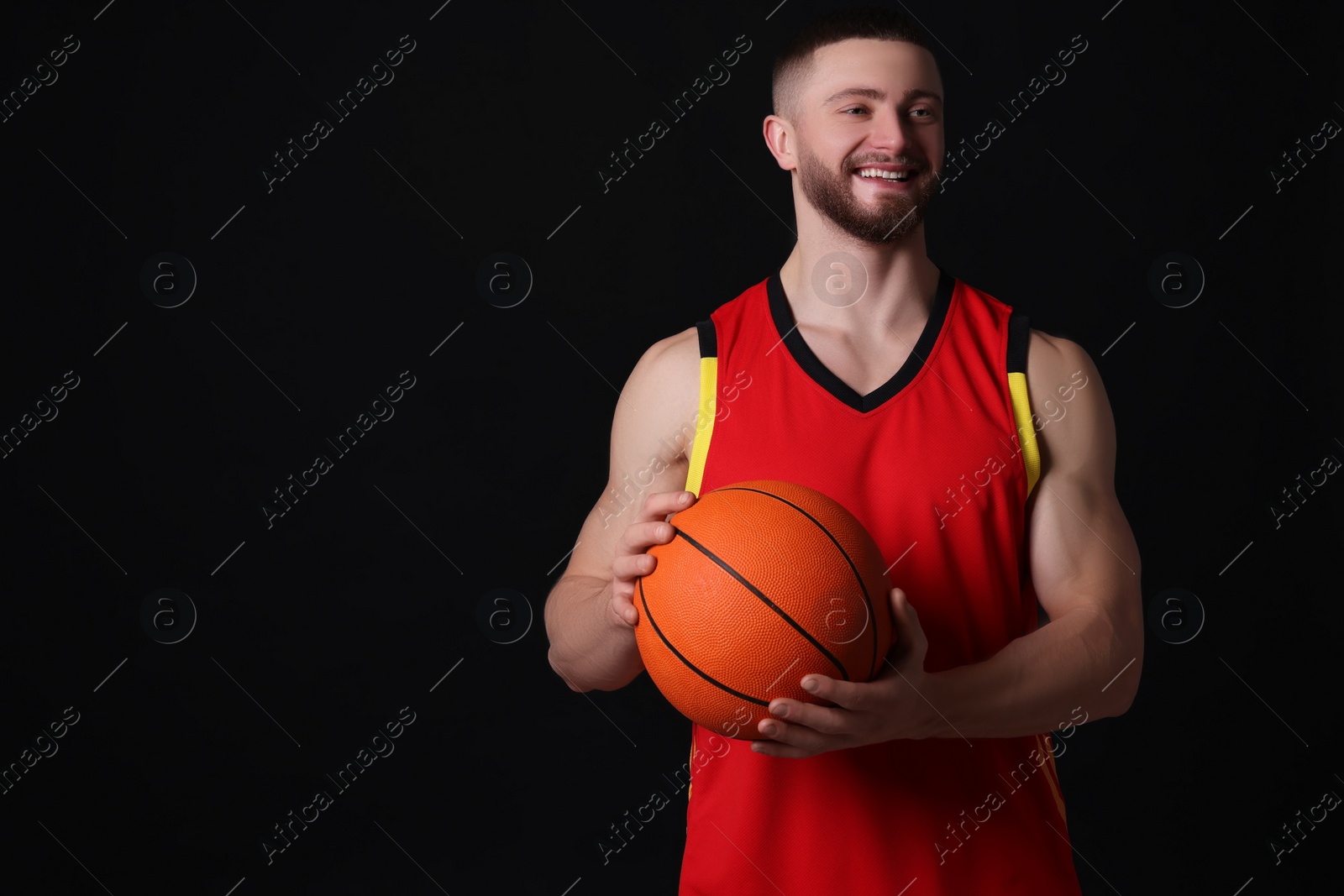 Photo of Athletic young man with basketball ball on black background. Space for text