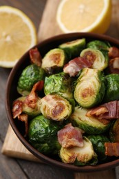 Delicious roasted Brussels sprouts and bacon in bowl on table, closeup