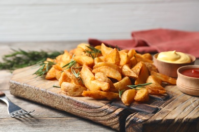 Photo of Baked potatoes served with rosemary, ketchup and mayonnaise on wooden board