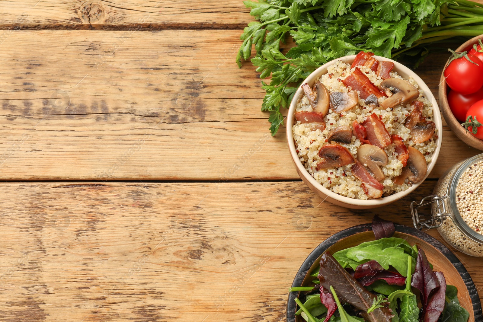 Photo of Tasty quinoa porridge with fried bacon, mushrooms in bowl and vegetables on wooden table, flat lay. Space for text