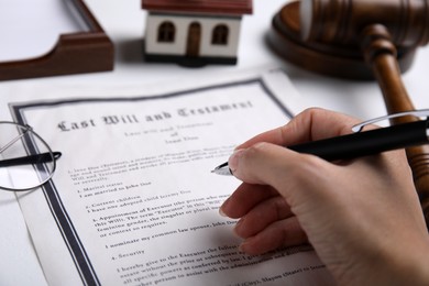 Woman signing last will and testament at white table, closeup