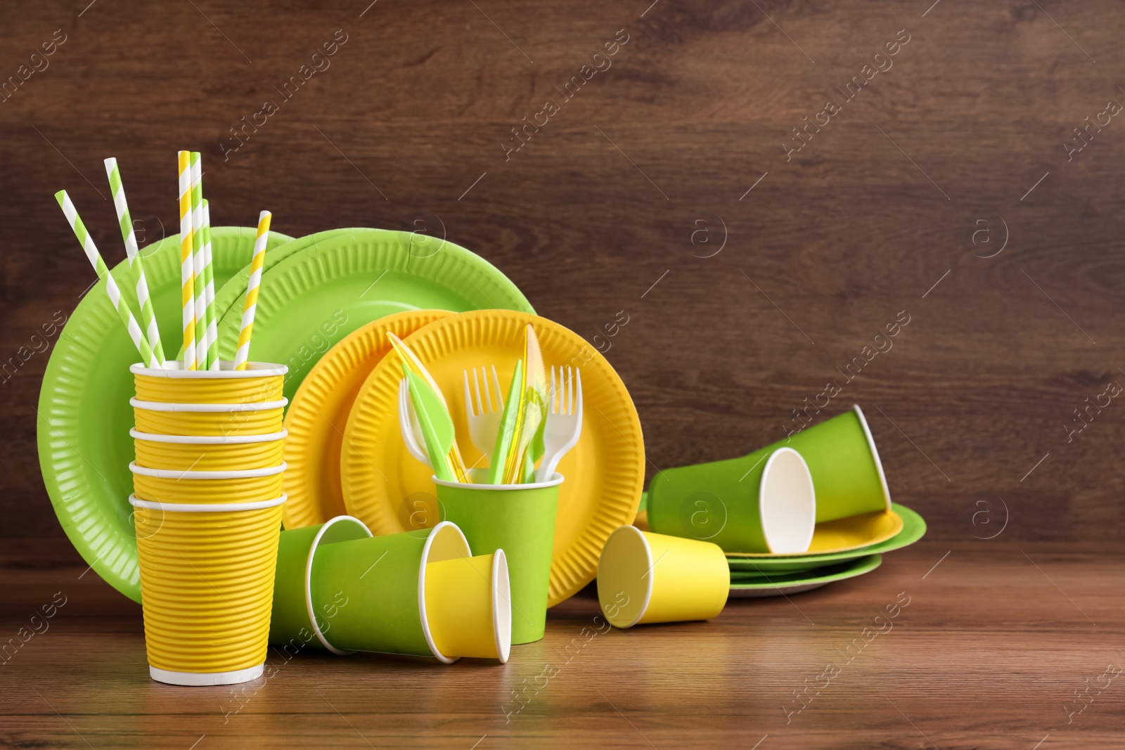 Photo of Set of bright disposable tableware on wooden table