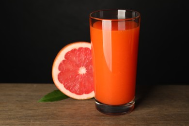 Photo of Tasty grapefruit juice in glass, leaf and fresh fruit on wooden table against black background, closeup
