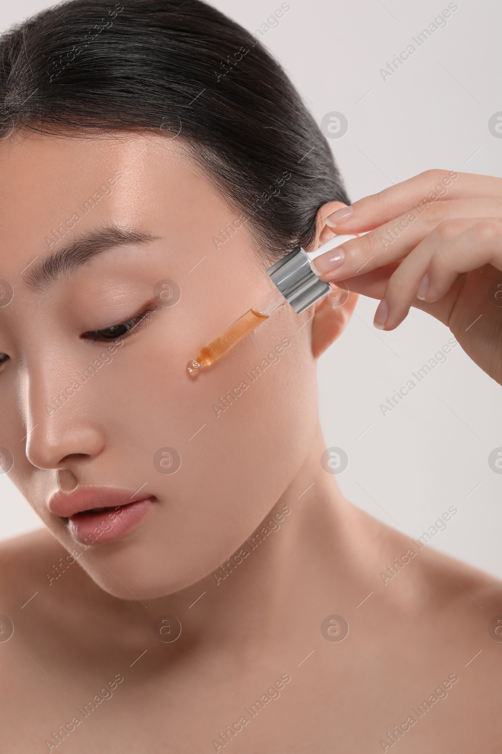 Photo of Beautiful young woman applying cosmetic serum onto her face on white background, closeup