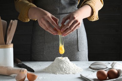 Photo of Woman beating egg into dough at table on dark background, closeup