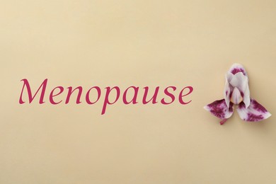 Photo of Word Menopause and orchid flower on beige background, top view