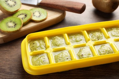 Photo of Kiwi puree in ice cube tray and ingredients on wooden table. Ready for freezing