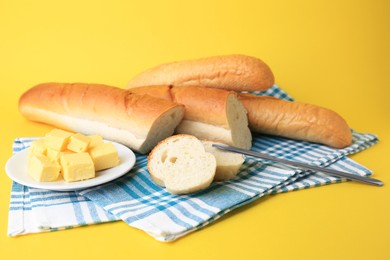 Photo of Whole and cut baguettes with fresh butter on yellow background