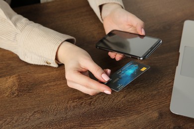 Photo of Online payment. Woman with smartphone using credit card at wooden table, closeup