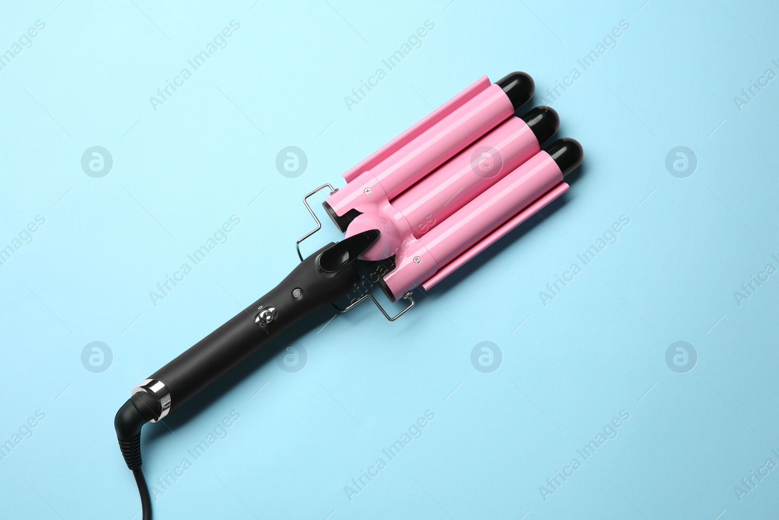 Photo of Modern triple curling hair iron on light blue background, top view