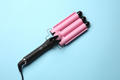 Modern triple curling hair iron on light blue background, top view