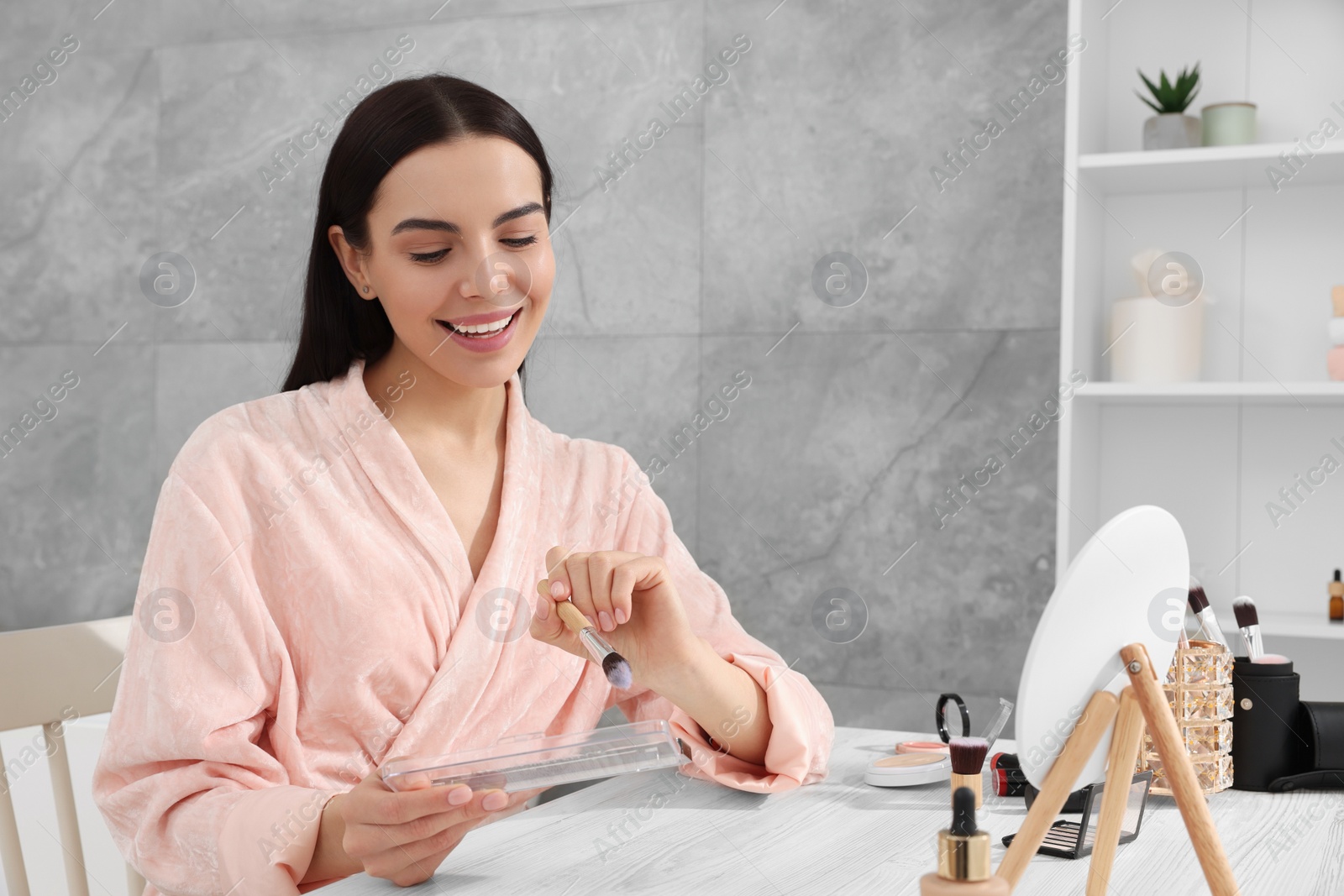 Photo of Beautiful young woman with blusher and brush at dressing table indoors. Space for text