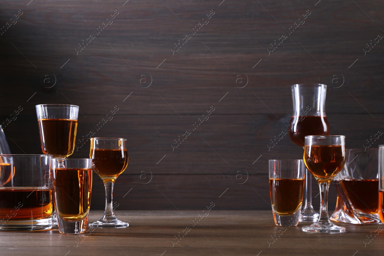 Photo of Different delicious liqueurs in glasses on wooden table, space for text