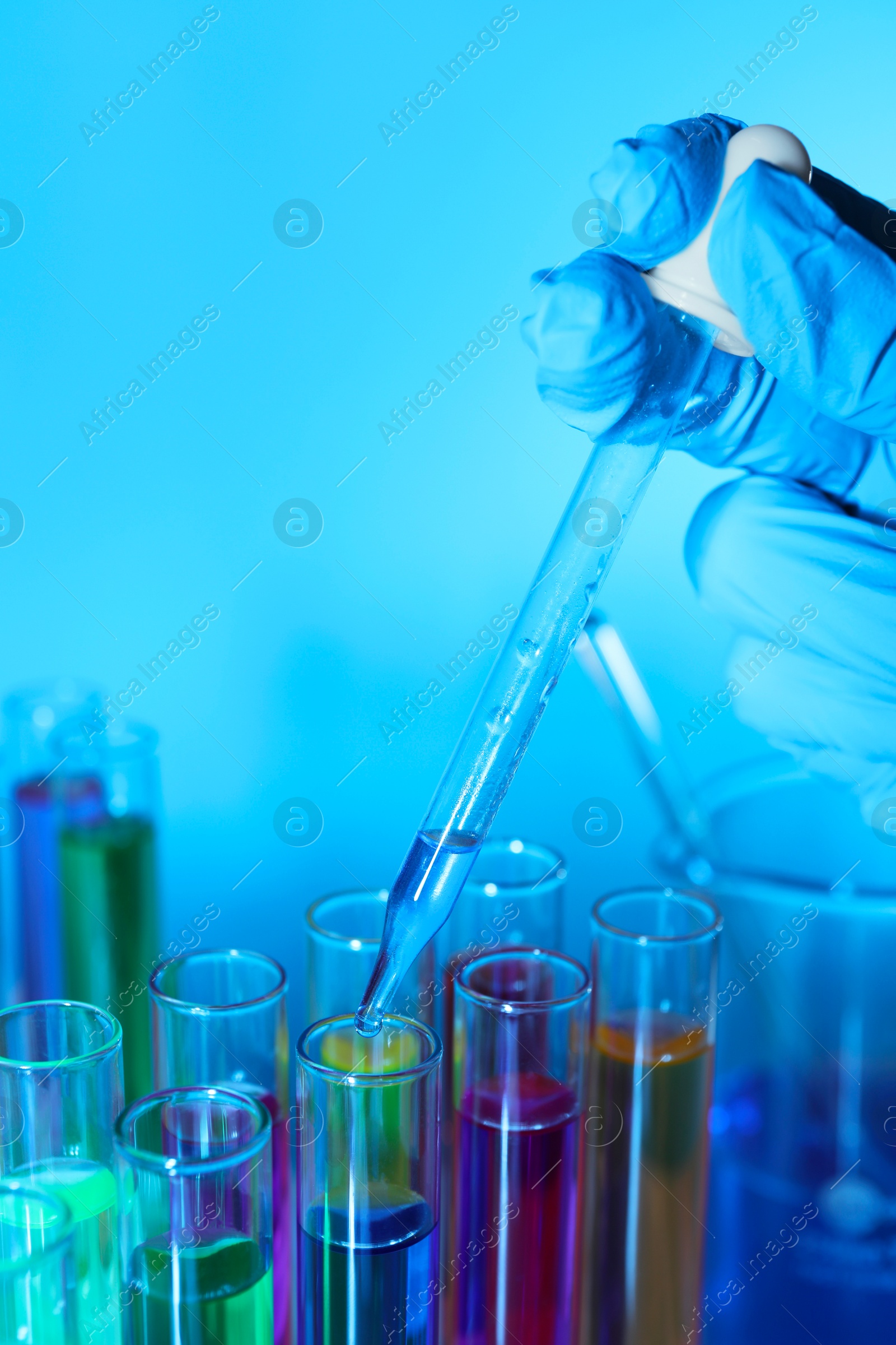 Photo of Scientist dripping liquid from pipette into test tube on light blue background, closeup