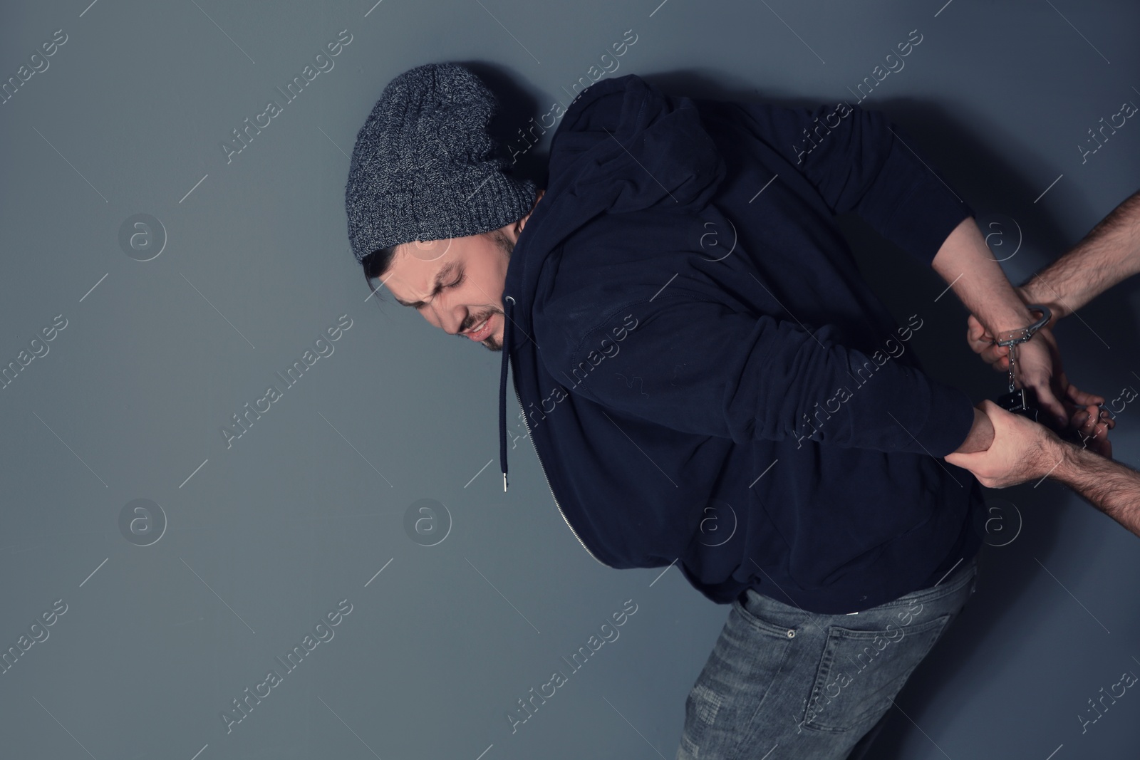 Photo of Man putting handcuffs on drug dealer against grey background. Space for text