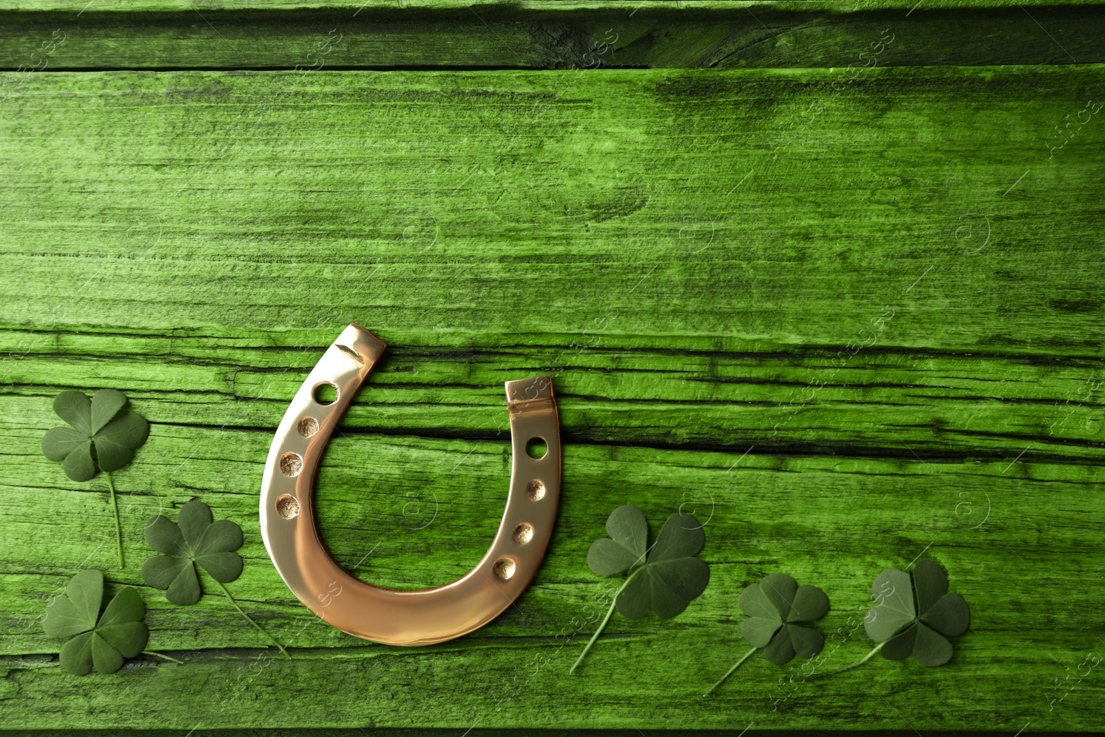 Image of Clover leaves and horseshoe on green wooden table, flat lay with space for text. St. Patrick's Day celebration