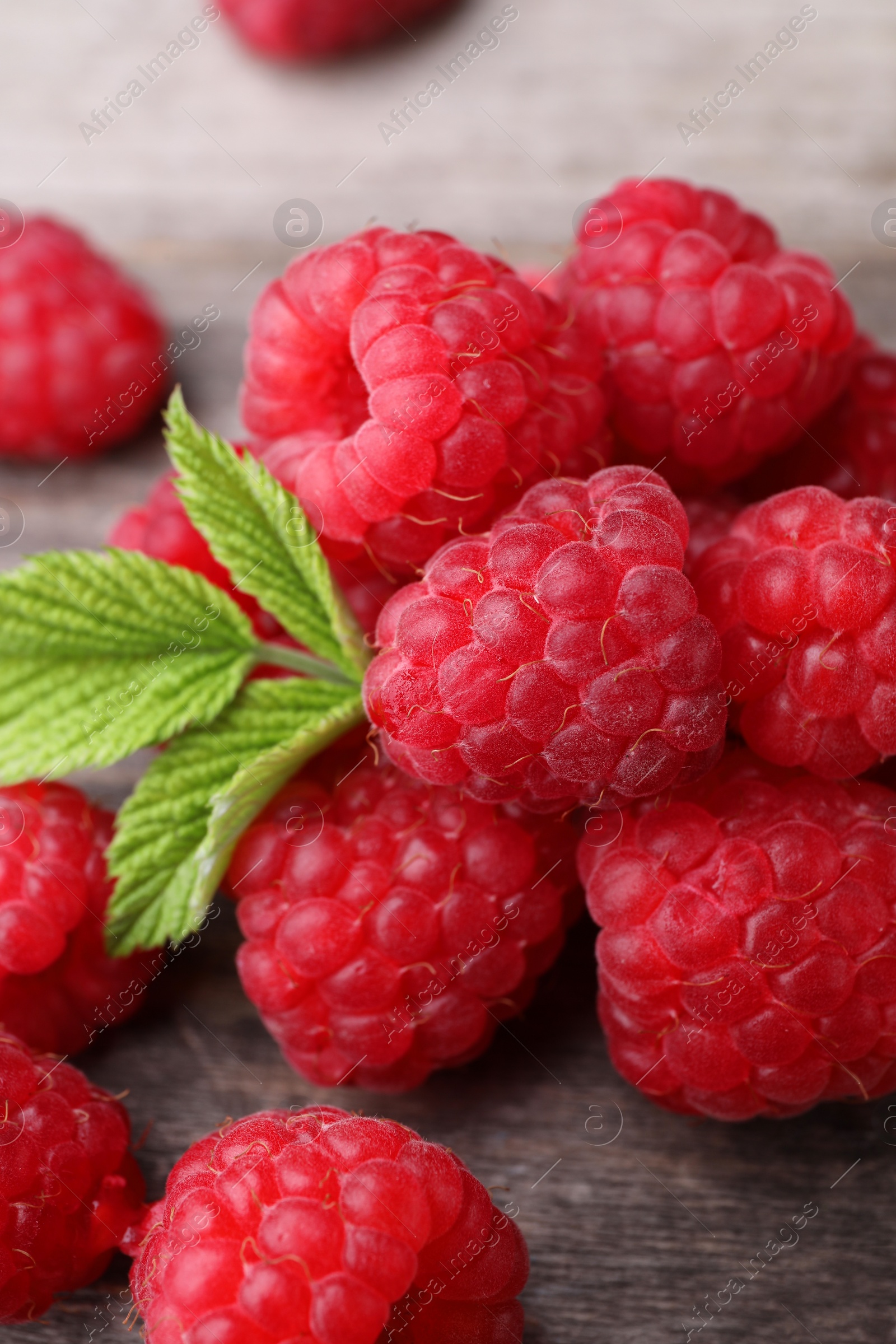 Photo of Tasty ripe raspberries and green leaves on wooden table, closeup