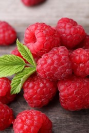Photo of Tasty ripe raspberries and green leaves on wooden table, closeup