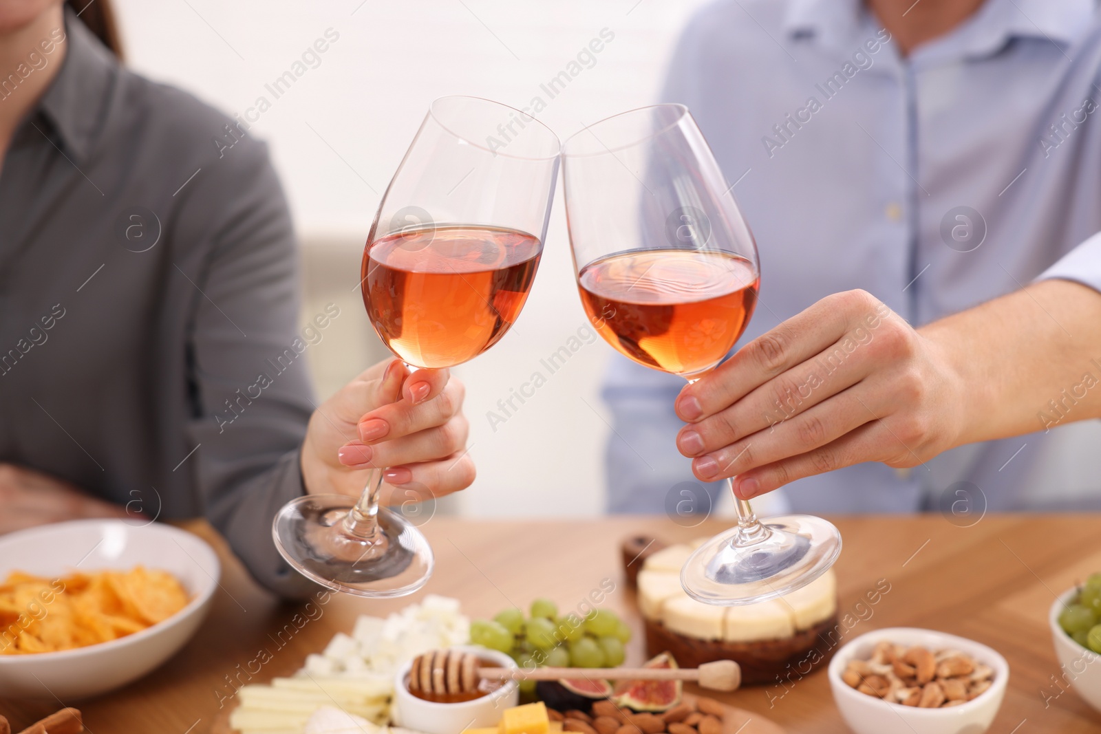 Photo of People clinking glasses with rose wine above wooden table indoors, closeup