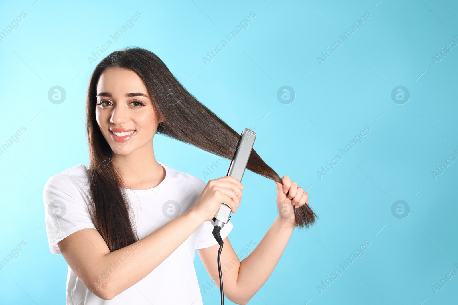 Photo of Happy woman using hair iron on color background. Space for text