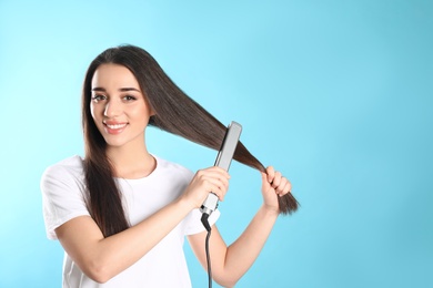 Happy woman using hair iron on color background. Space for text