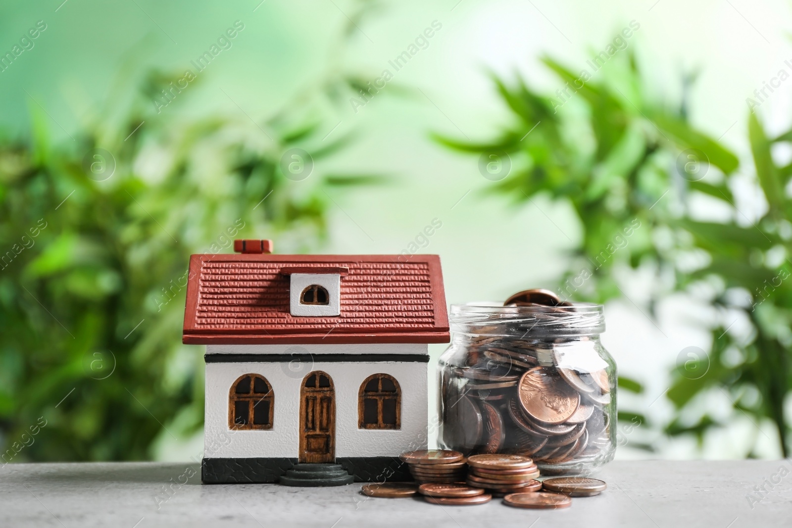 Photo of House model and jar with coins on table against blurred background. Space for text