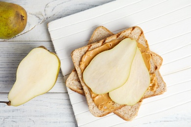 Photo of Slice of bread with peanut butter and pear on white wooden table, flat lay