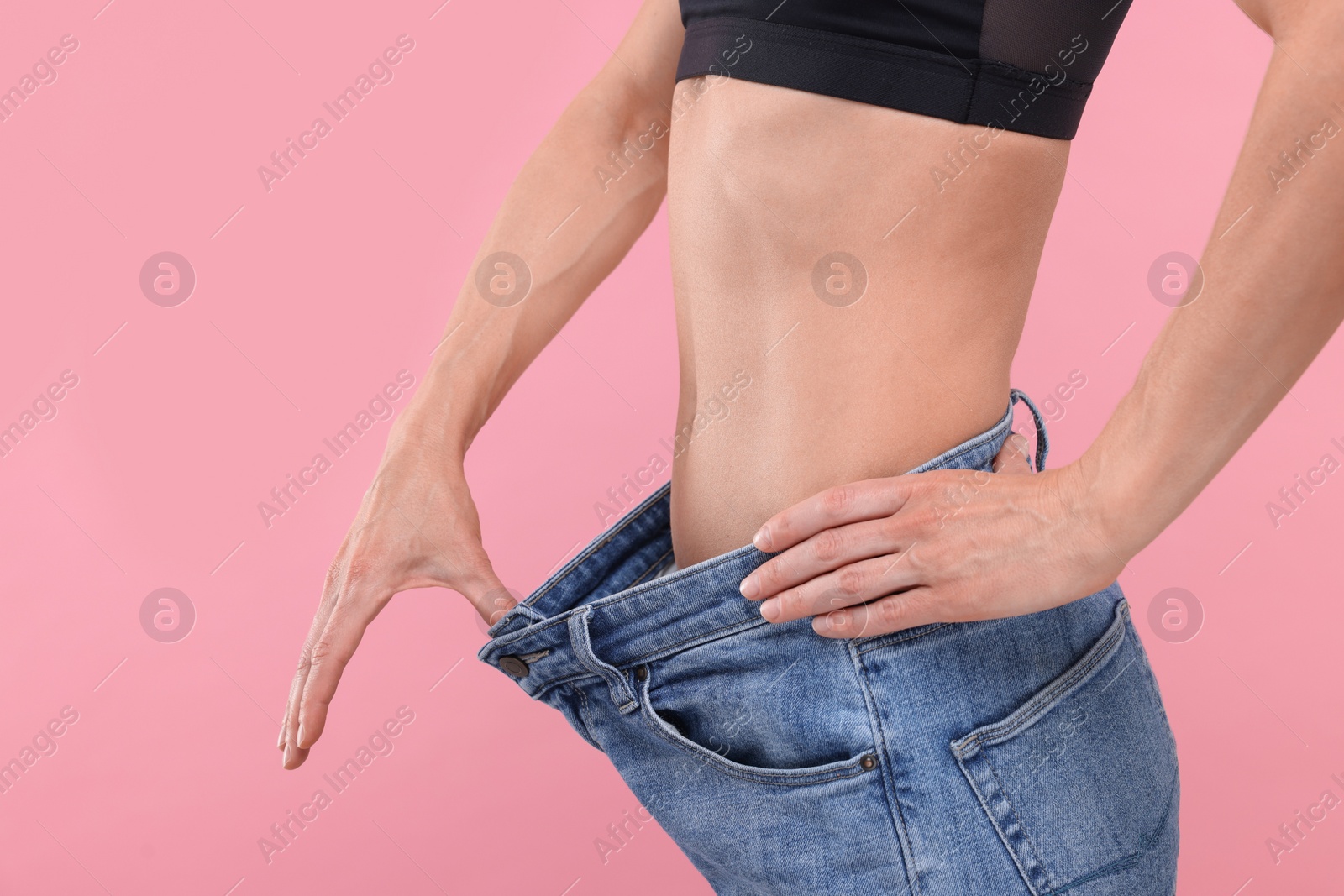 Photo of Slim woman wearing big jeans on pink background, closeup. Weight loss