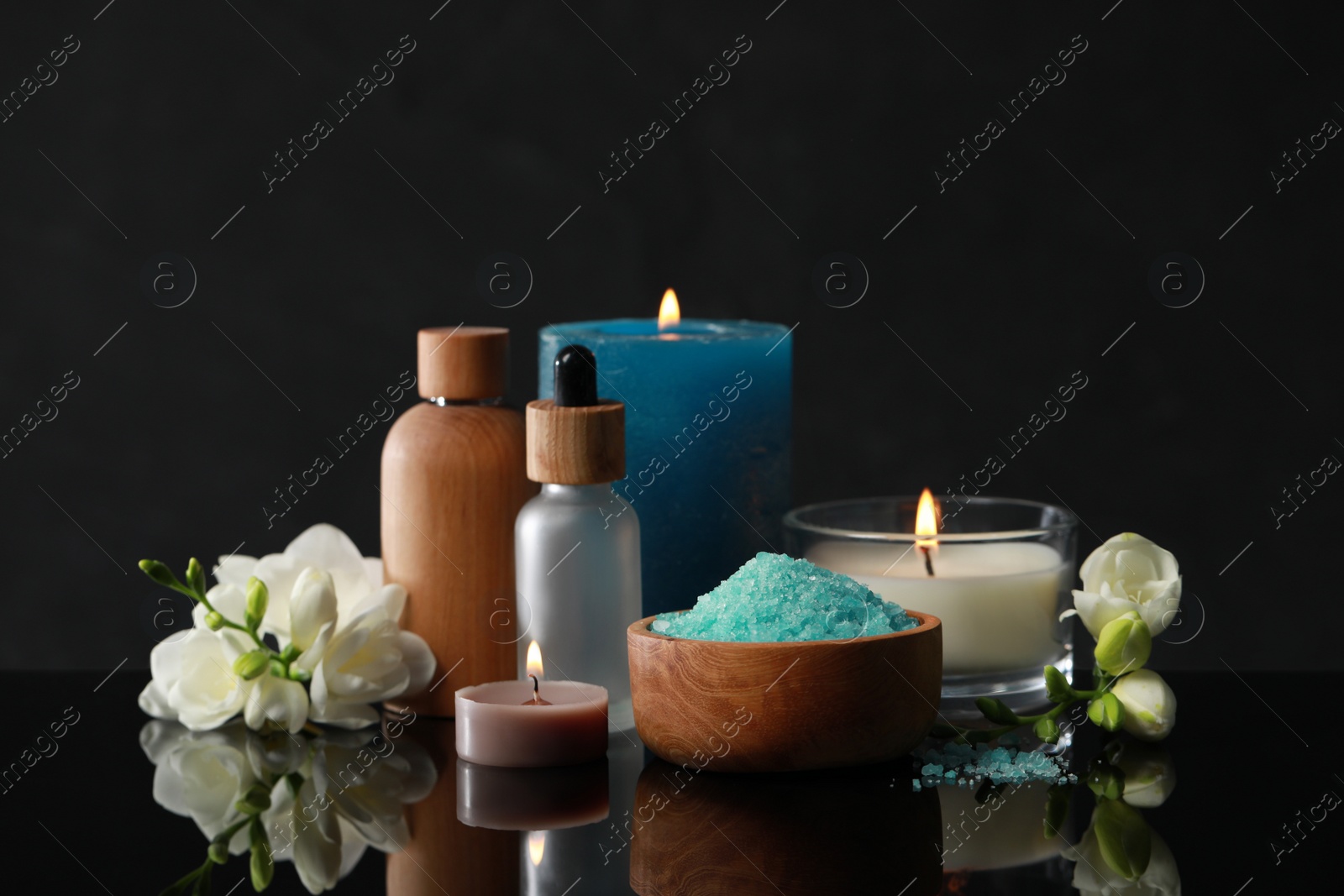 Photo of Beautiful spa composition with different care products, burning candles and flowers on black mirror surface