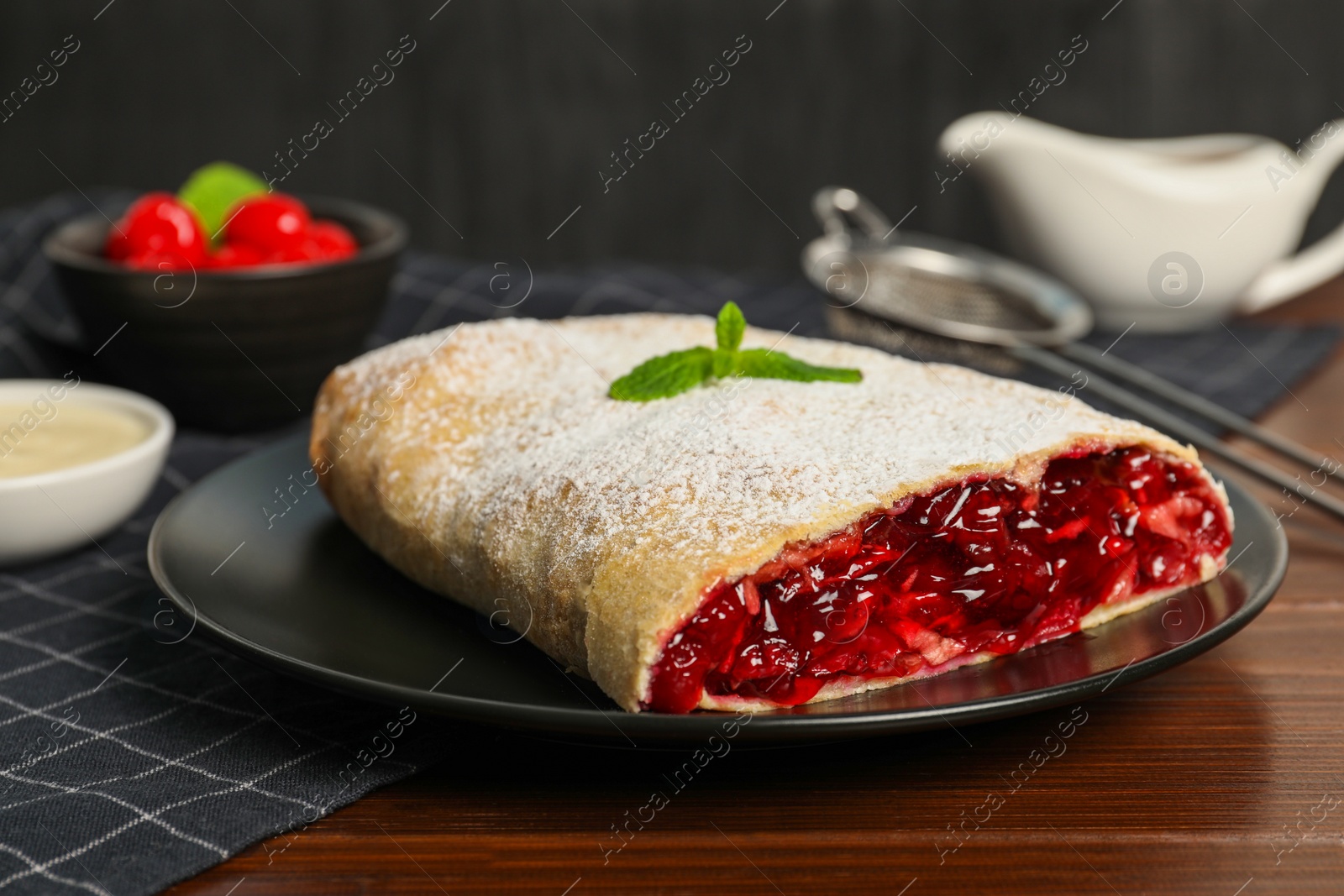 Photo of Delicious strudel with cherries, powdered sugar and mint on wooden table, closeup