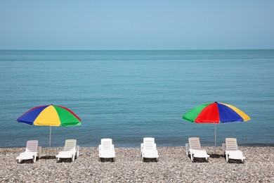 Beautiful view of umbrellas and sunbeds on pebble beach near sea