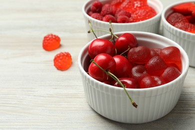 Photo of Delicious gummy candies and fresh fruits on white wooden table, closeup. Space for text