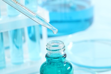 Dripping liquid from pipette into bottle on blurred background, closeup. Laboratory analysis