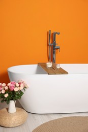 Stylish bathroom interior with ceramic tub and beautiful bouquet of roses