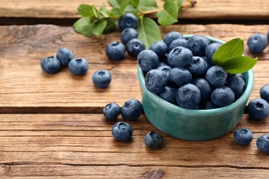 Photo of Tasty fresh blueberries and green leaves on wooden table, space for text