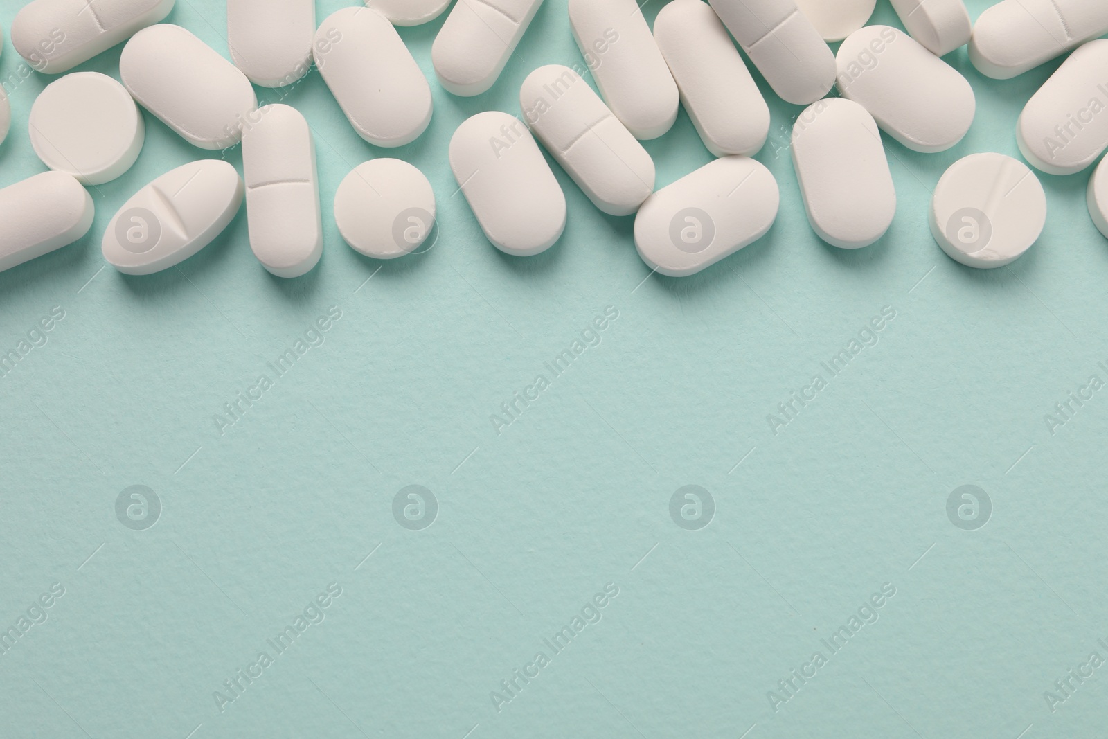 Photo of Many white pills on mint background, flat lay. Space for text