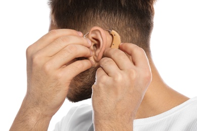 Young man putting hearing aid in ear on white background