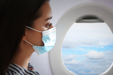 Traveling by airplane during coronavirus pandemic. Woman with face mask near porthole