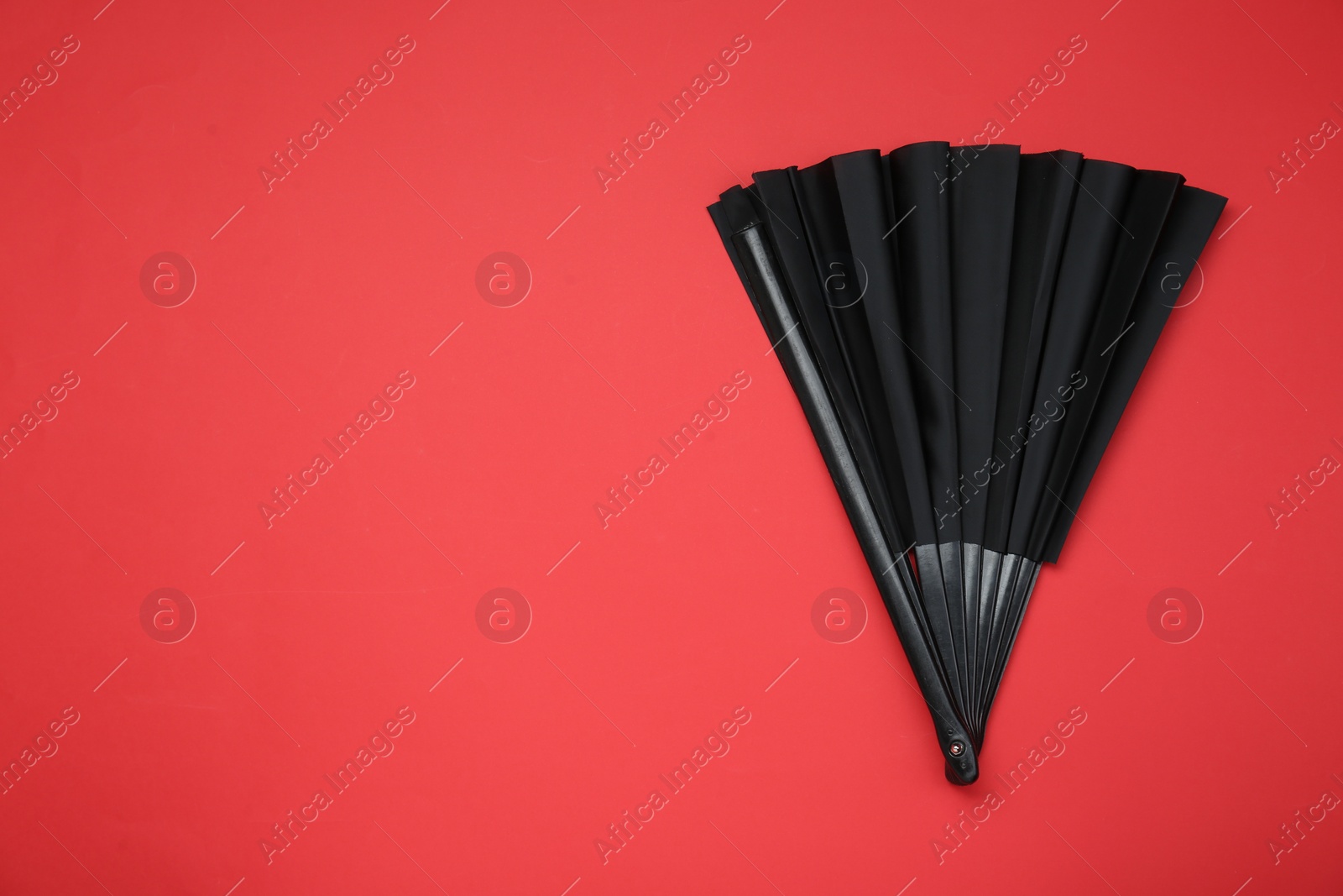 Photo of Stylish black hand fan on red background, top view. Space for text